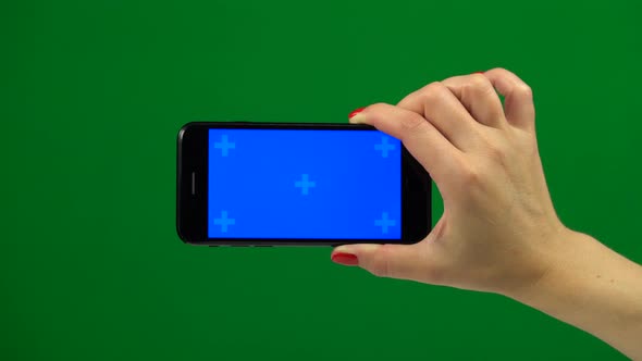 Hand Holding a Blue Screen Smartphone Over a Green Screen