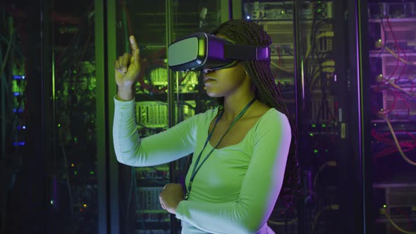 African american female computer technician using vr headset working in business server room