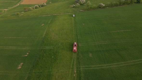 aerial shot of a tractor with spraying materials leaving the huge green meadows after his work