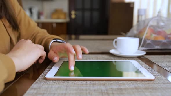 Girl checks e-mails on a tablet while drinking tea in her kitchen