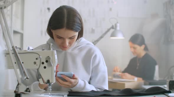 Woman Seamstress Looks at the Smartphone Screen in the Workplace