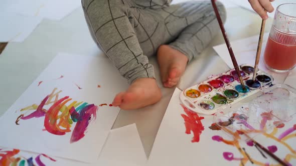 little boy of two years old draws with paints sitting on the floor