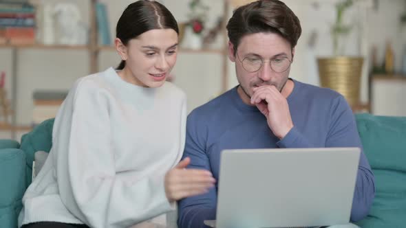 Hispanic Couple Working on Laptop Together While Sitting on Sofa