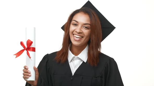 African American Young Graduate Female in Black Academic Dress Holding Her Diploma and Showing Ok