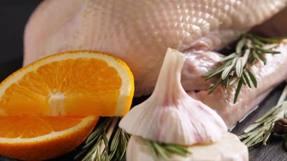 Raw Organic Whole Duck with Cut Orange and Rosemary on Slate Board on Black Background