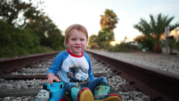 A young child has a great time playing on the train tracks pretending to be an engineer.