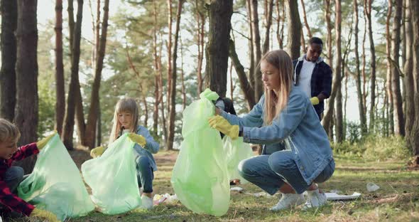 Multiracial Adults Together with Children Collecting Garbage Into Plastic Bags from Park Territory