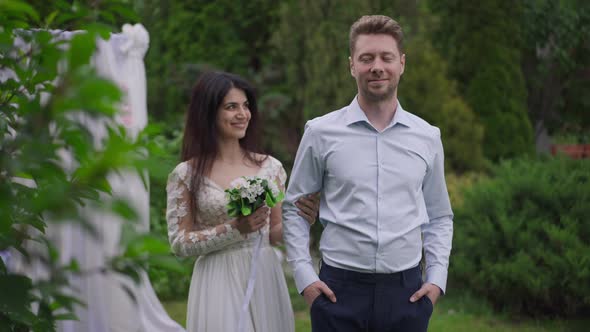 Charming Middle Eastern Bride Walking to Happy Caucasian Groom Posing in Spring Garden Outdoors