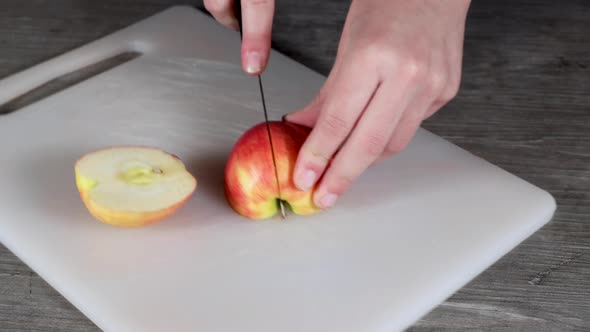 A young woman in a kitchen cutting up a red apple on a plastic chopping board