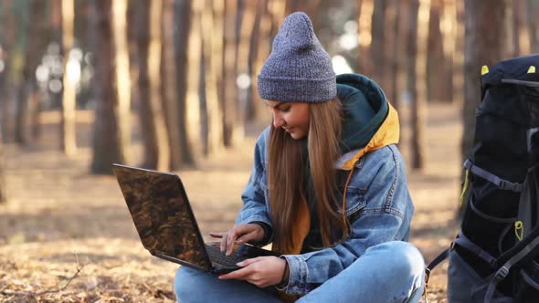 Young attractive girl sitting near a large hiking backpack and uses laptop