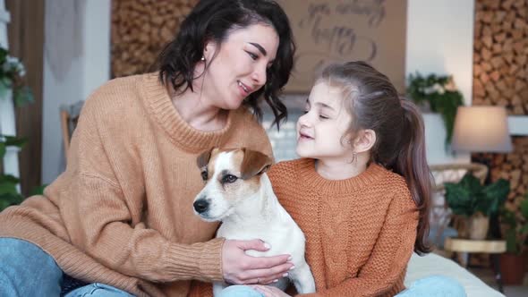 Young Mother Daughter in Knitted Sweaters are Sitting on a Bed in a Cozy Bedroom with Their Small