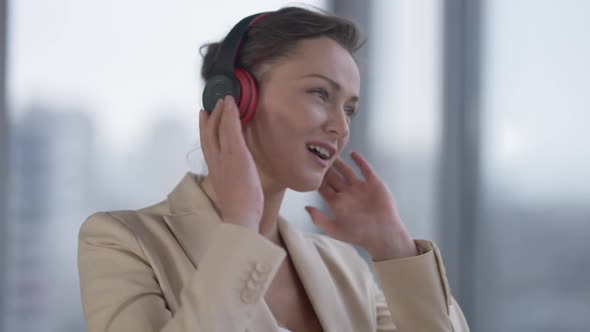 Positive Slim Beautiful Woman in Headphones Enjoying Music Dancing at Window