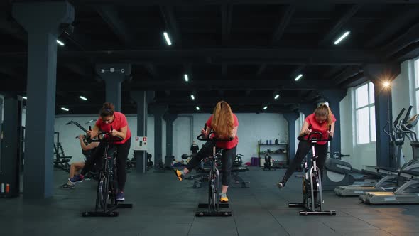 Group Athletic Girls Performing Aerobic Riding Training Exercises on Cycling Stationary Bike in Gym