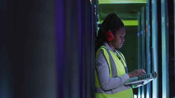 African american female computer technician using laptop working in business server room