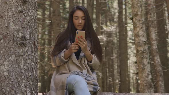 Pretty Woman Using Phone in Forest Sitting on Wooden Log