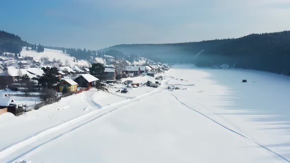 Aerial View of a Village with Wooden Houses on the Bank of a Frozen River in Winter