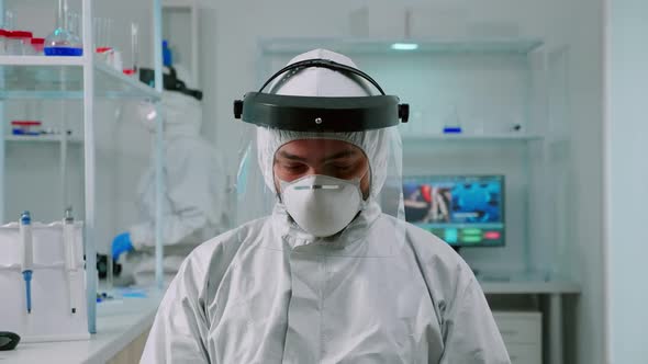 Chemist in Coverall Looking Up at Video Camera Sitting in Lab