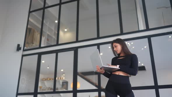 Young Woman Holding Laptop in Hands and Browsing Internet at Home