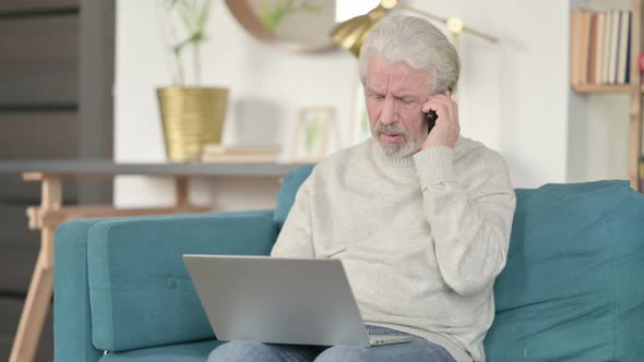 Old Man with Laptop Talking on Smartphone on Sofa 