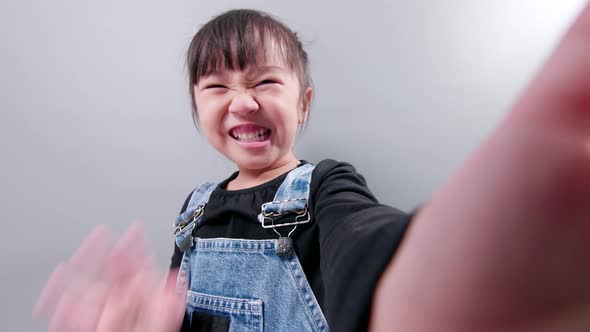 Happy little asian girl using smartphone for video call, waving hand and speaking and talking with s