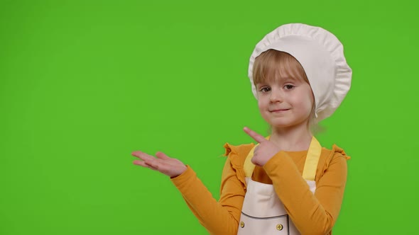 Child Girl Dressed Like Chef Cook Pointing at Left on Blank Space Place for Your Advertisement Logo