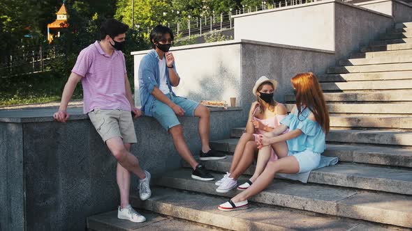 Young Multiethnic Friends in Black Protective Masks are Talking and Laughing While Having Rest on