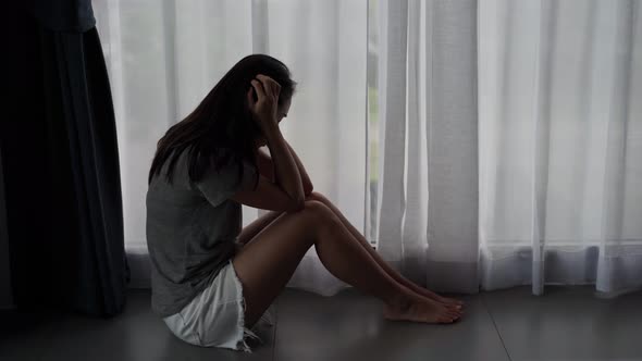 Lonely young woman feeling depressed and stressed sitting in the dark bedroom