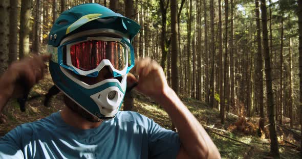 Medium shot, downhill biker is wearing a blue full face helmet, trees in the background.