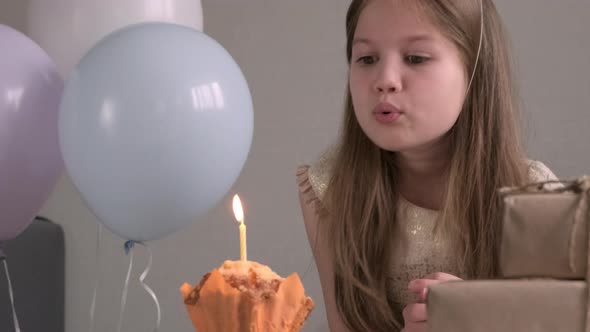 Close Up Cute Little Girl in Party Hat Blows Out the Candle on the Birthday Cupcake