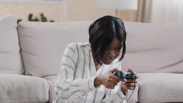 Young Focused Happy African American Woman Sitting in Living Room Playing Console Uses Controller