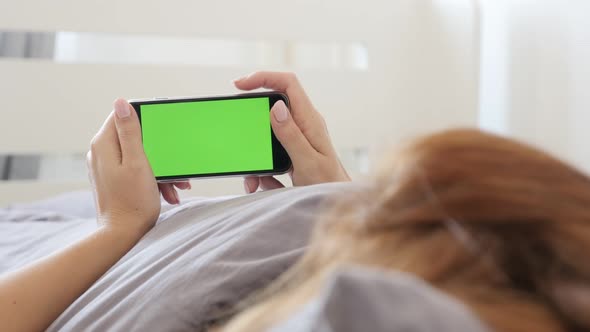 Female relaxing in bed while holds green screen gadget 4K 2160p 30fps UltraHD footage - Greenscreen 