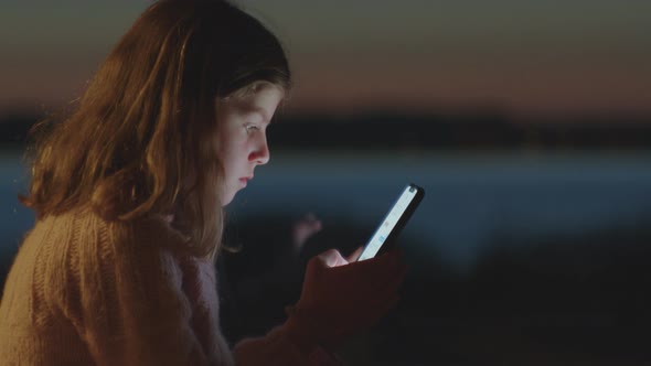 Young Girl Playing On Smartphone At Dusk