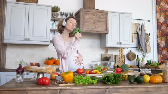Beautiful Pregnant Woman Singing In Broccoli And Dancing In Headphones On Kitchen.