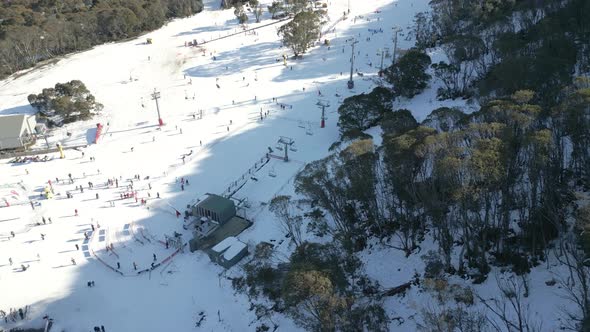 Aerial view of a busy alpine snow resort with many winter activities. People skiing, snowboarding, c