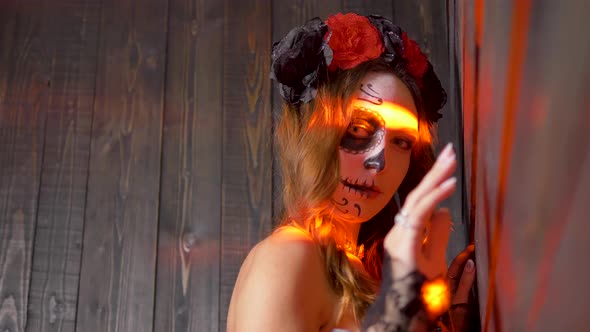 Portrait of a Woman with Halloween Makeup on Her Face in Red Rays of Light Beckons with Her Fingers