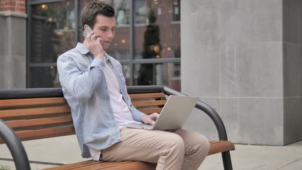 Young Man Talking on Phone while Sitting on Bench