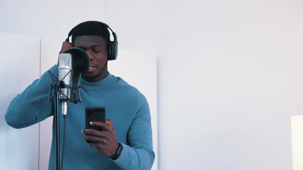 Man Wearing Headphones Singing a Song Into a Microphone in a Studio