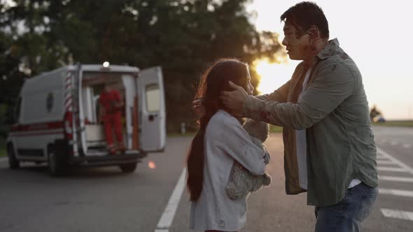 Father Hugging Daughter While Paramedics Helping Mother