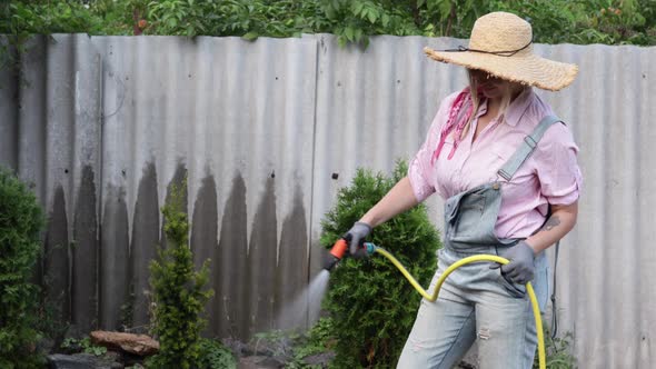 A Young Adult Woman Wateres a Vegetable Garden with a Garden Hose Outside the House