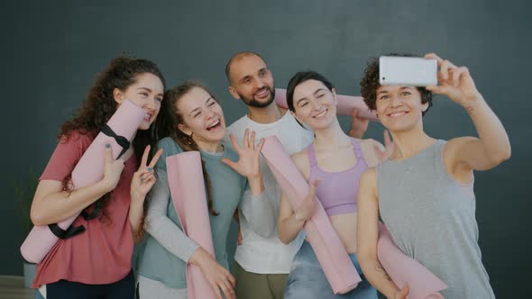 Cheerful Young People Taking Selfie in Yoga Studio Holding Mats Using Smartphone Camera