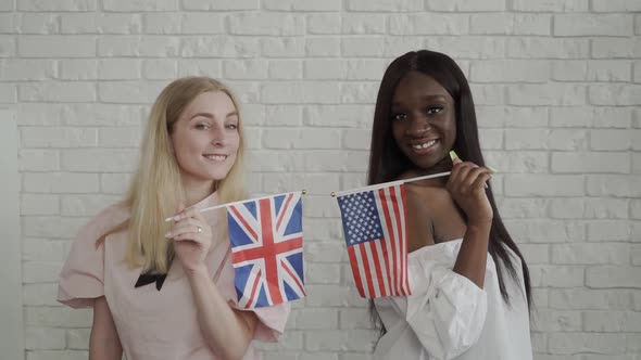 Young Women Holding British and American Flags Smiling at Each Other. Caucasian and African American