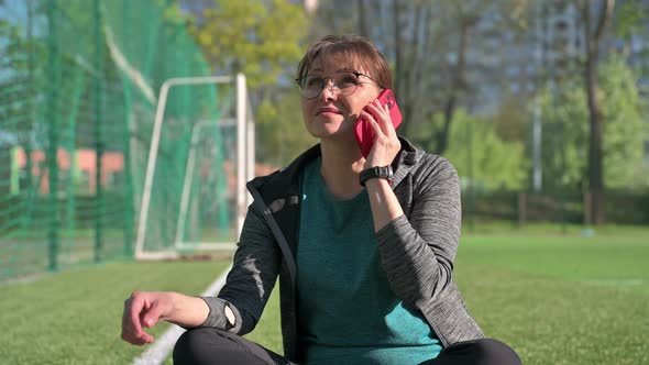 Middle Aged Woman in Sportswear Talking on the Phone While Sitting at Sports Outdoor Stadium