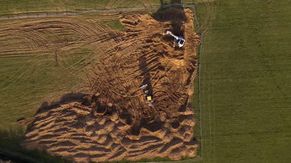 Sandy construction site in its beginning state with two excavators and one person approaching them.