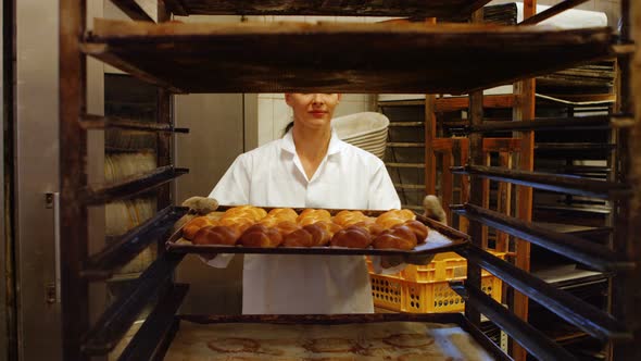 Female baker putting baked michetta in baking trolley