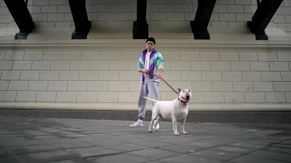 Portrait of Hipster Guy and His Dog Holding Purebred Bullterrier on Leash While Standing Over