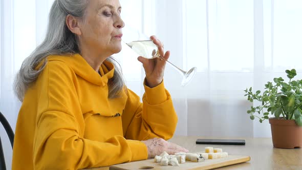 Beautiful Old Grandmother with Grey Hair and Face with Wrinkles Sitting at the Table at Home on