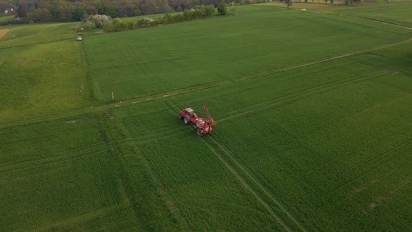 aerial footage of a tractor unfolding its sprinkler system in a huge green meadow