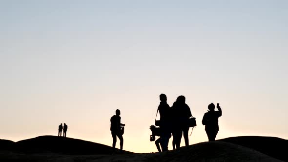 Wide shot of people in silhouette against a pink sky in the Namib desert at sunset