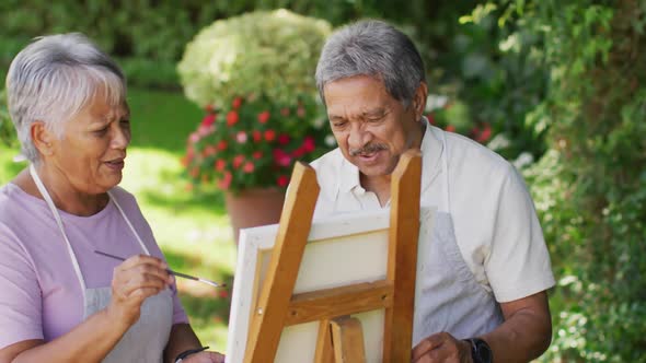 Video of happy biracial senior couple painting in garden