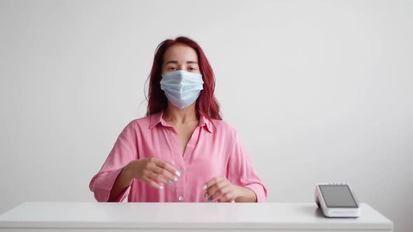 Woman Administrator in Medical Mask Stands Behind Reception and Invites Clients